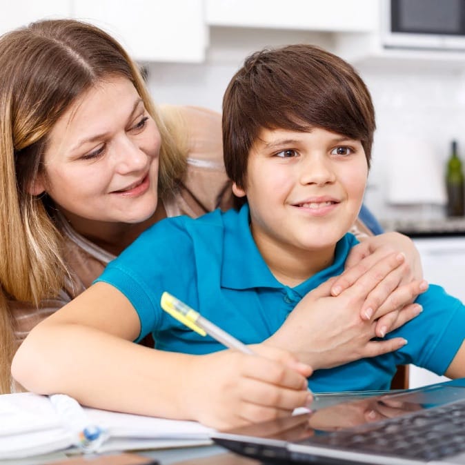 Boy doing homework with smiling mother hugging him from behind